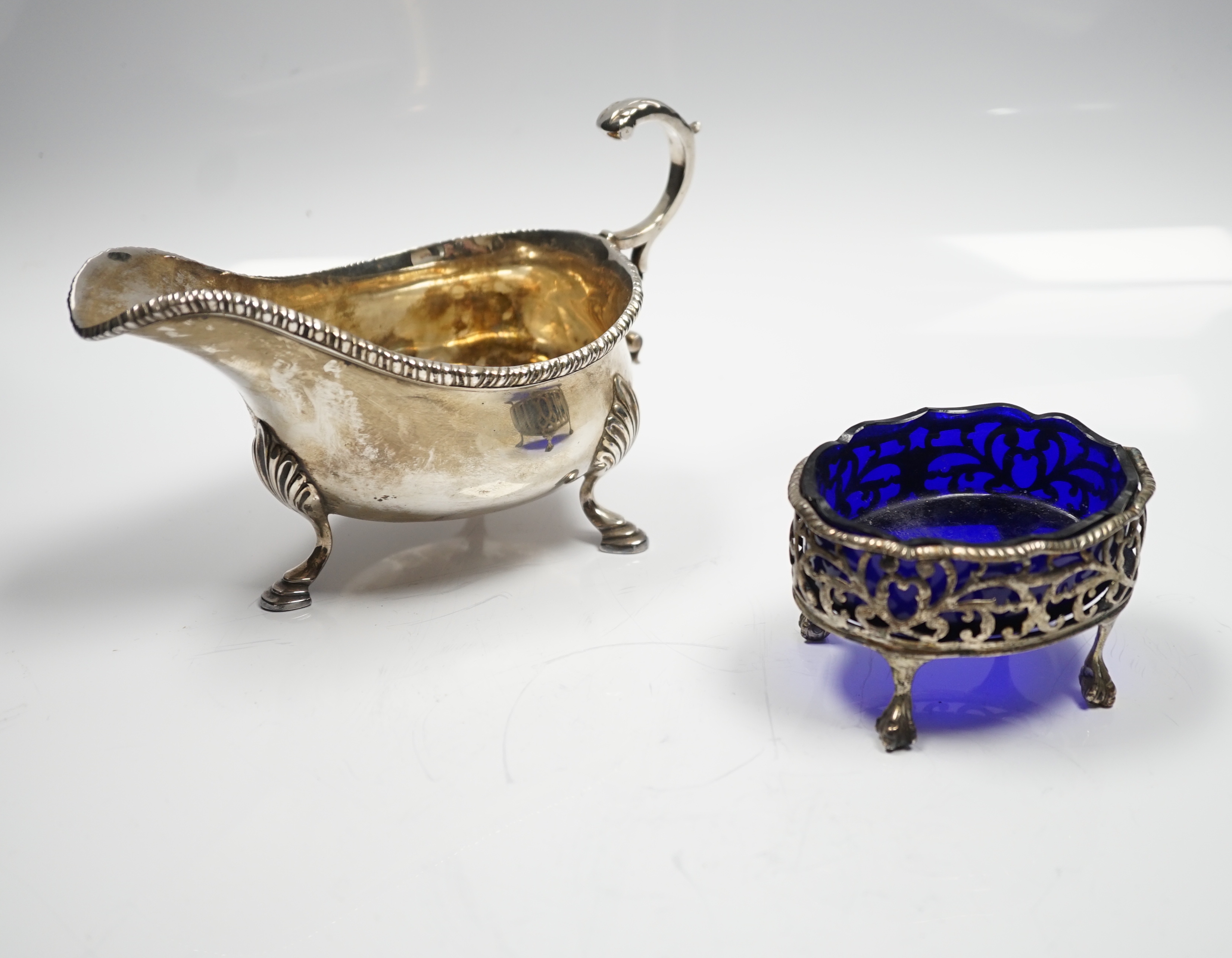 A late Victorian silver sauceboat, with flying scroll handle, William Hutton & Sons, London, 1898 and a George III pierced silver oval salt, with blue glass liner, London, 1768, 12.2oz.